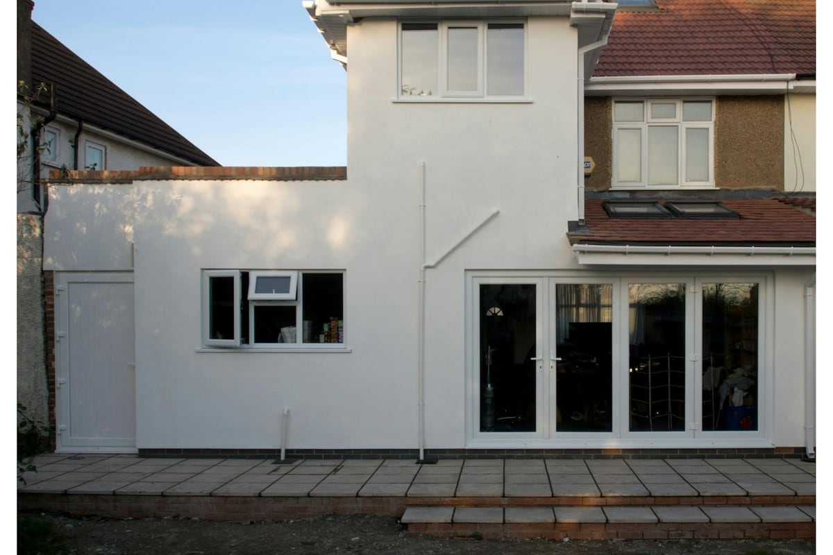 The same house finished, a rendered two-storey extension with new patio doors and a paved patio