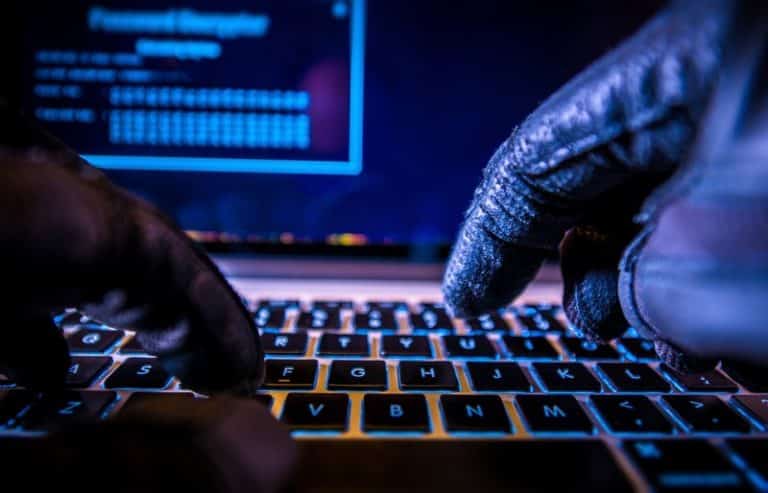 mains de hackers tapant sur le clavier d'un ordinateur éclairé par une lumière bleue