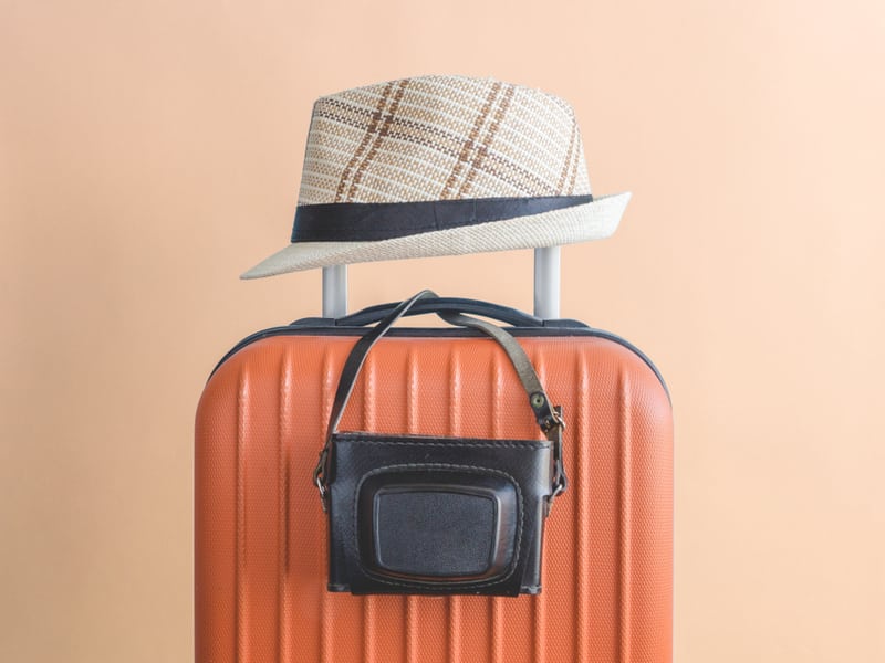 valise orange sur laquelle est posée un chapeau et un appareil photo